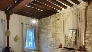 A rustic dining room with a stone wall, wooden beams, a fireplace, and a chandelier. - Appartement Authentique Dans le Centre de Caen (Caen)