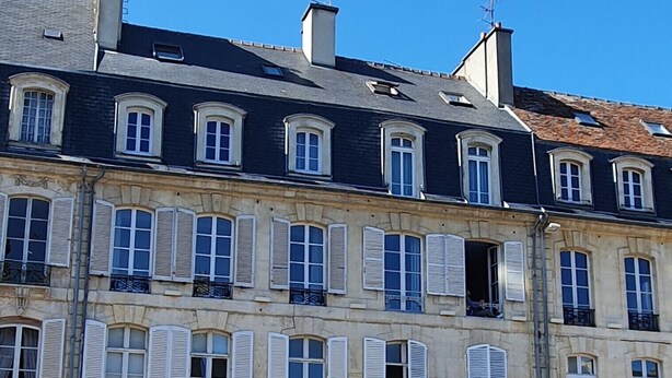 A multi-story building with a classic European architectural style, featuring a row of windows with shutters, a green door, and a parked car in front. - Appartement Authentique Dans le Centre de Caen (Caen)