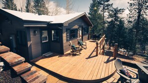 A cabin with a wooden deck, a covered porch, and a view of surrounding trees.
