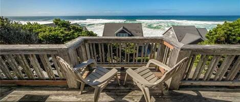 A wooden deck with two lounge chairs facing a view of the ocean.
