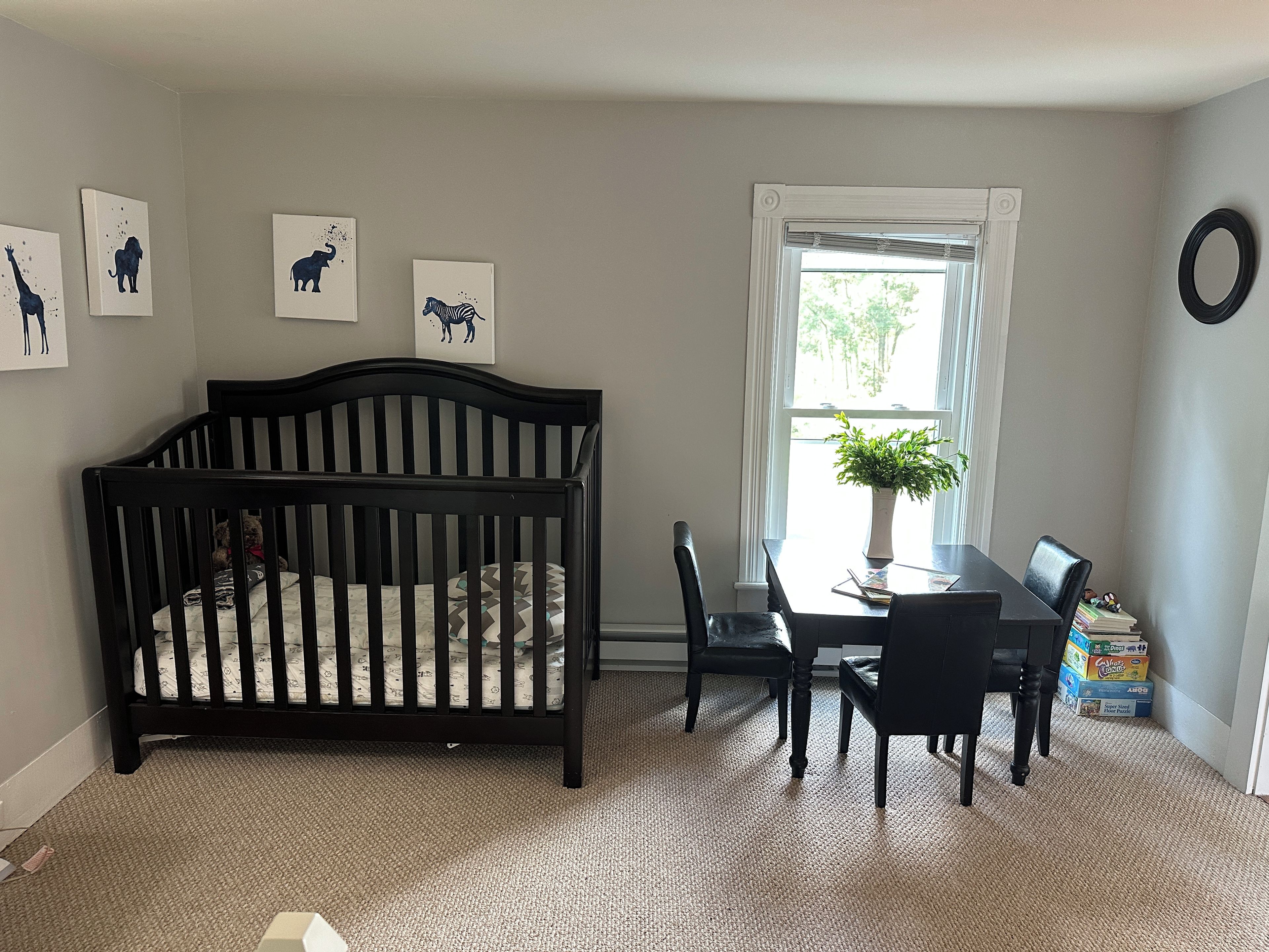Ein Zimmer mit einem Kinderbett, einem Esstisch mit Stühlen, einer Topfpflanze und Wandbildern.