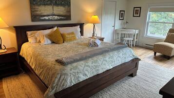 A bedroom with a large bed, a nightstand, a desk, a chair, a window, and a painting on the wall.