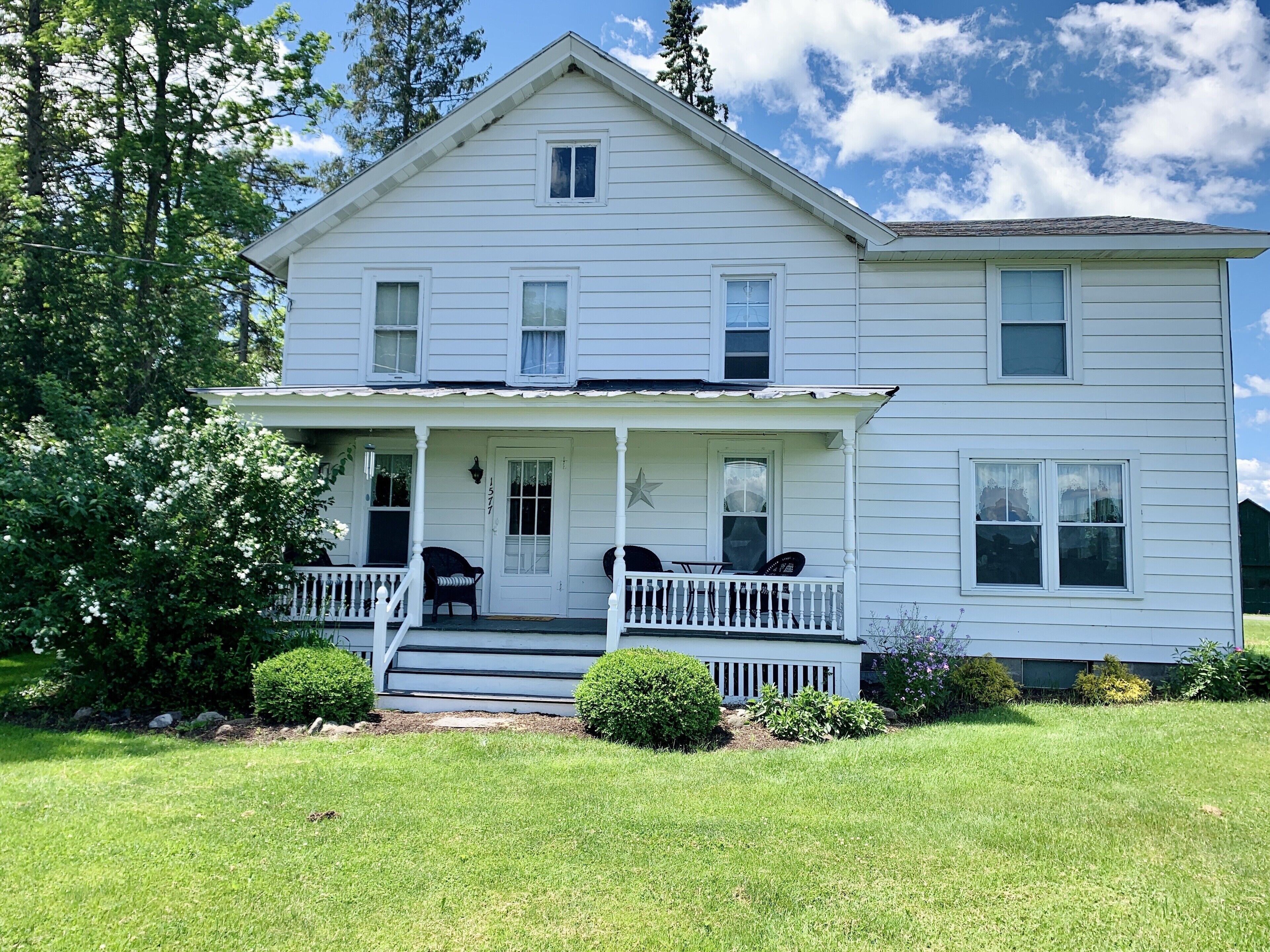 A two-story white house with a front porch, a small deck, and a mailbox.
