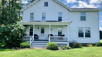 A two-story white house with a front porch, a small deck, and a mailbox.