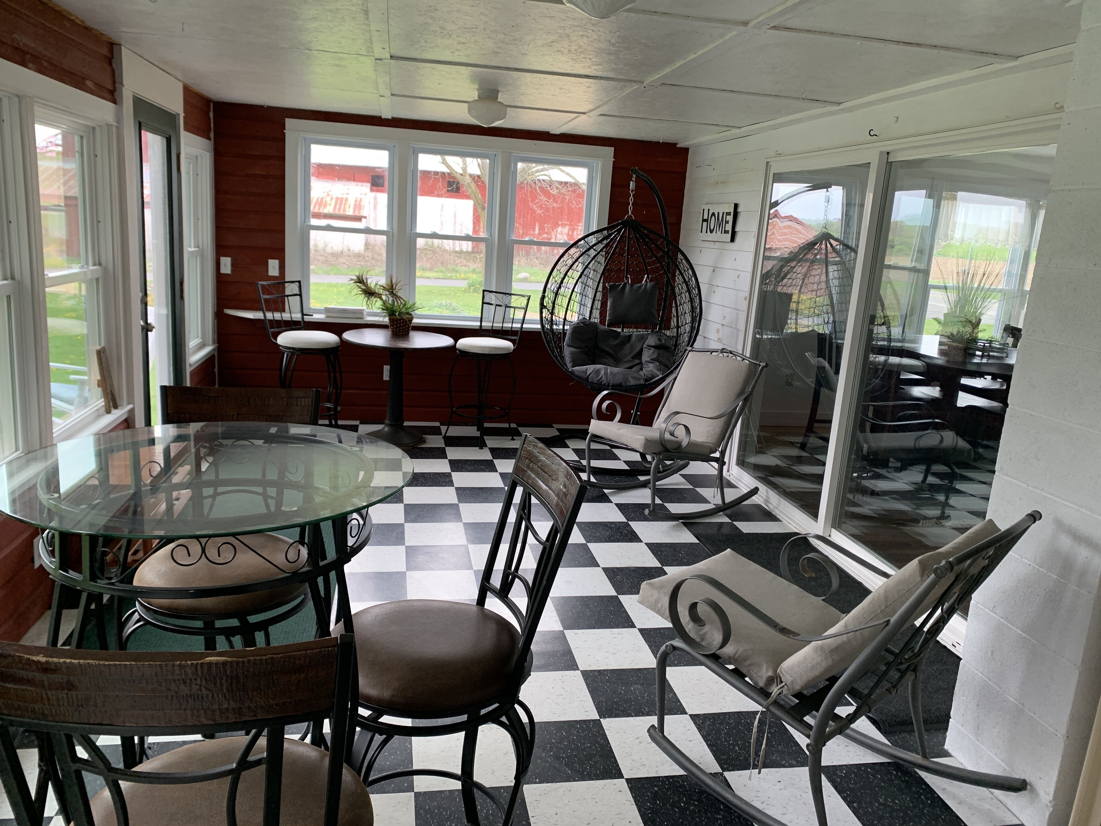 Un espace repas avec une table en verre, un sol à carreaux noirs et blancs et un fauteuil suspendu.