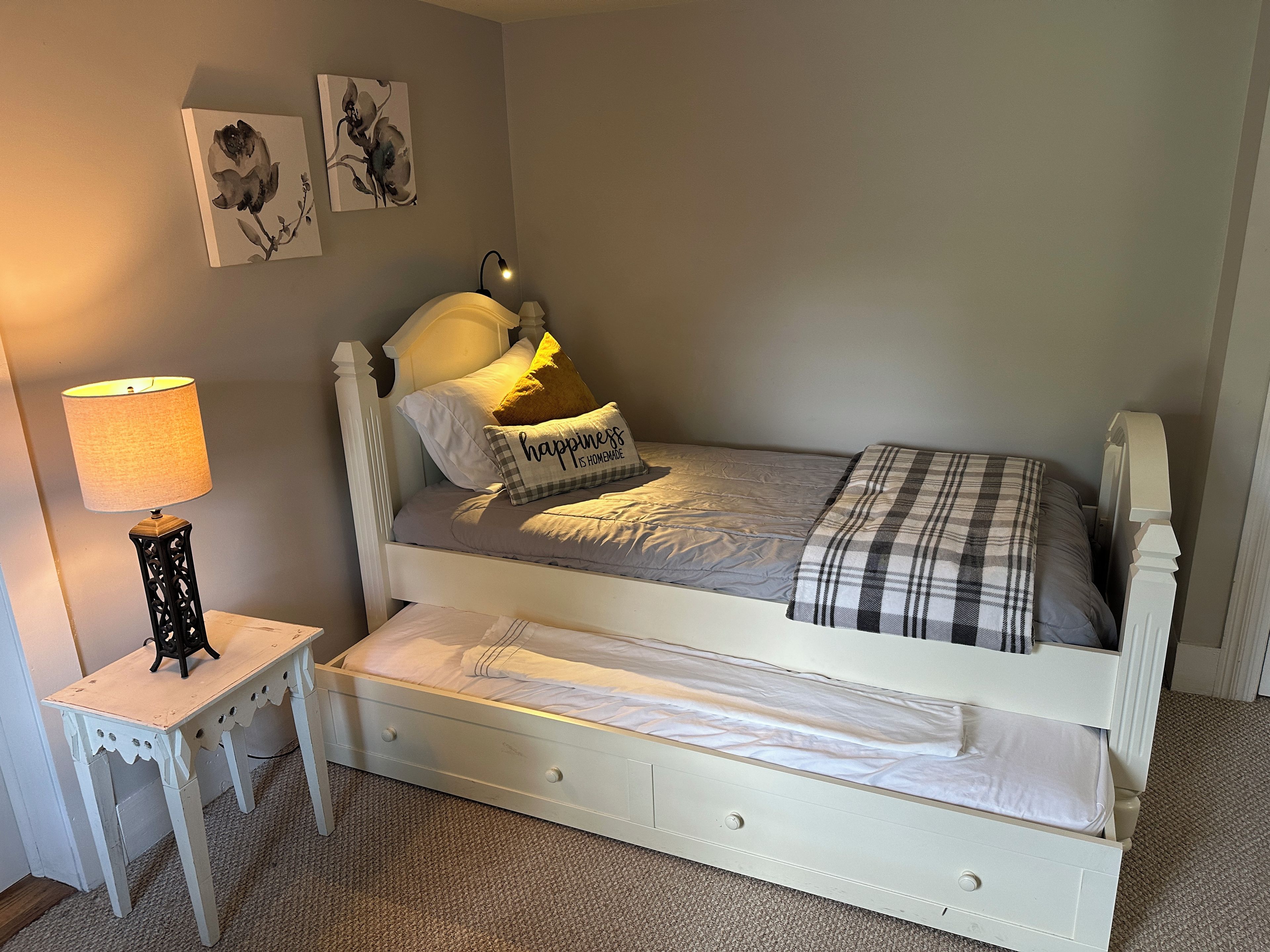 A single-bed room with a white headboard, a bedside table with a lamp, and a small drawer.