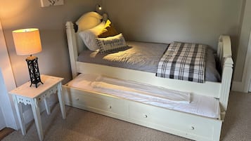 A single-bed room with a white headboard, a bedside table with a lamp, and a small drawer.