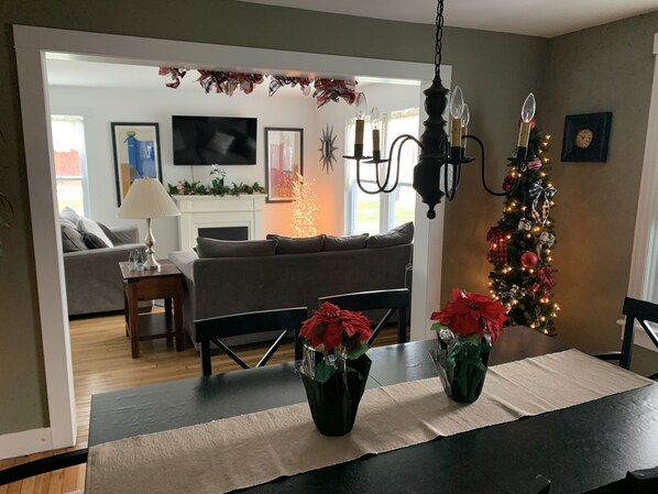 A dining area with a table set for two, a Christmas tree, and a living room in the background. - The Farmhouse - 2 ml from Colgate, king bed, family friendly, sleeps 10 (Hamilton)