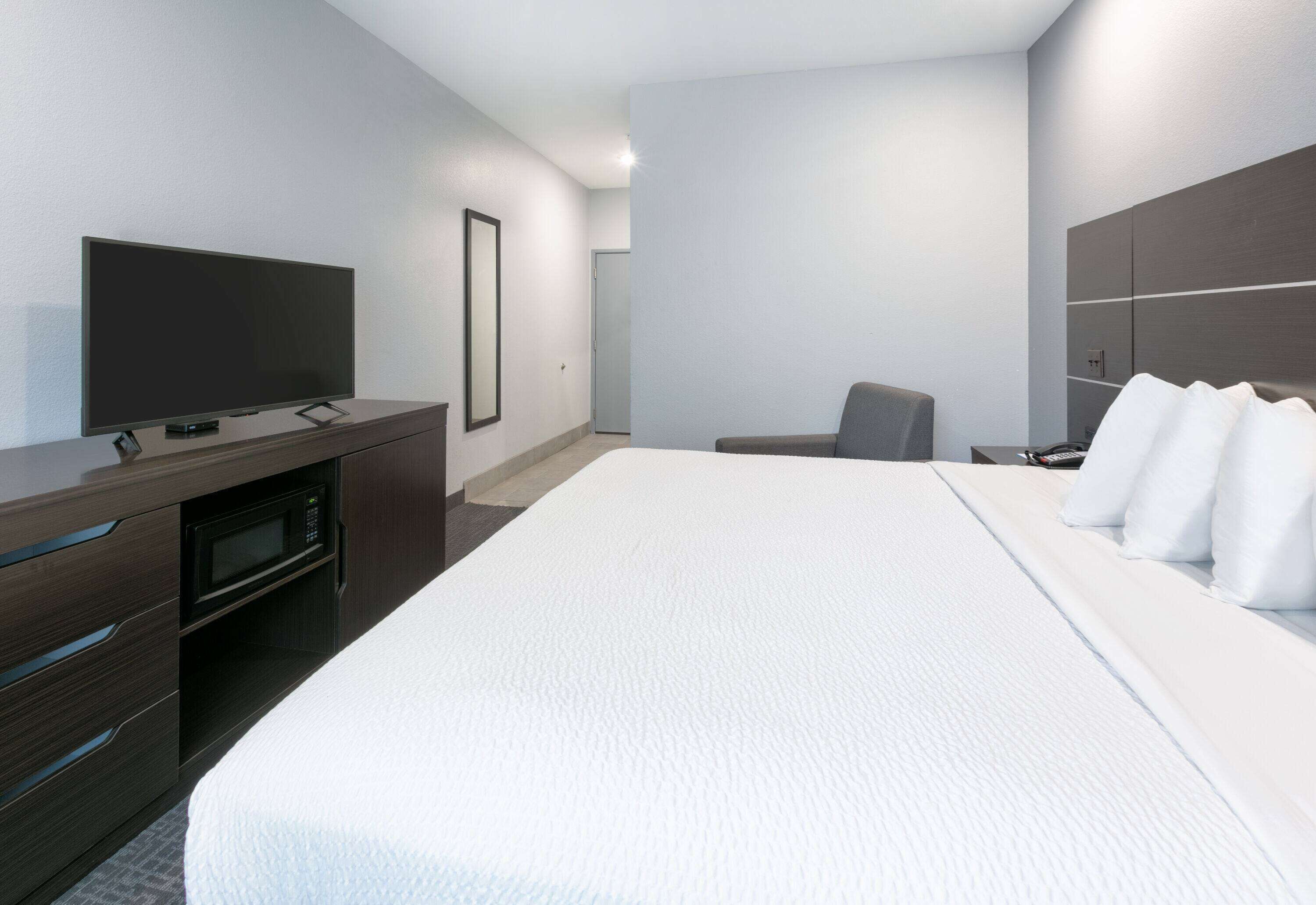 A modern hotel room with a large bed, a flat-screen TV, a microwave, and a desk with drawers.
