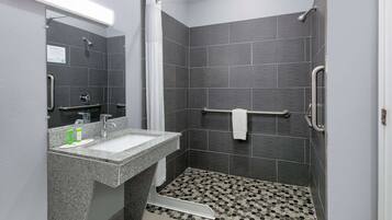 Een moderne badkamer met een granieten wastafel, een spiegel, een douche met een handdouche en een betegelde vloer met een honingraatpatroon.