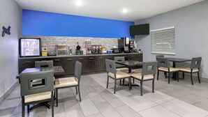 Una cocina moderna con una pared azul de acento, un comedor con seis sillas y un televisor de pantalla plana montado en la pared.