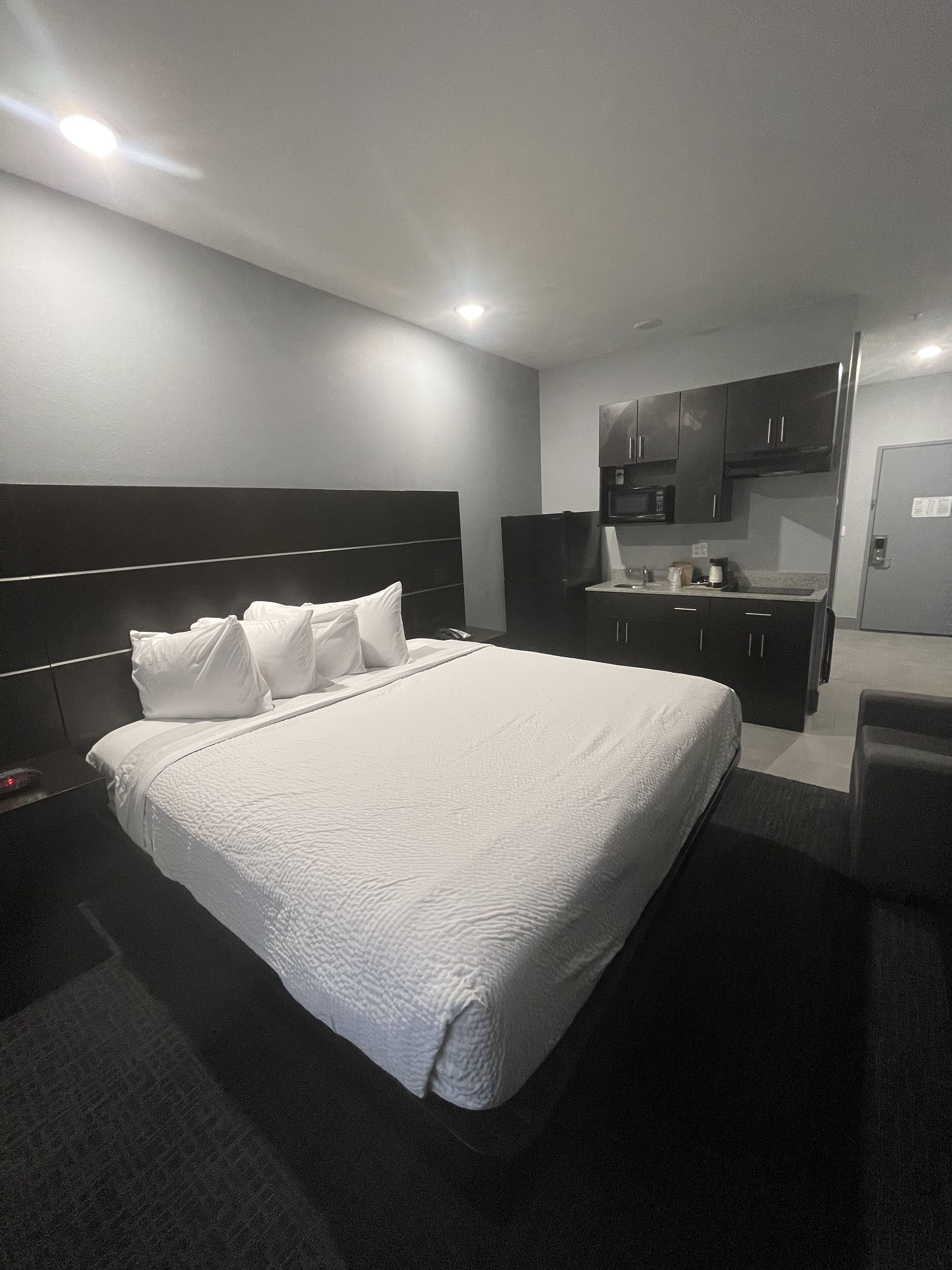 A modern hotel room with a large bed, a separate kitchenette, and a small seating area.