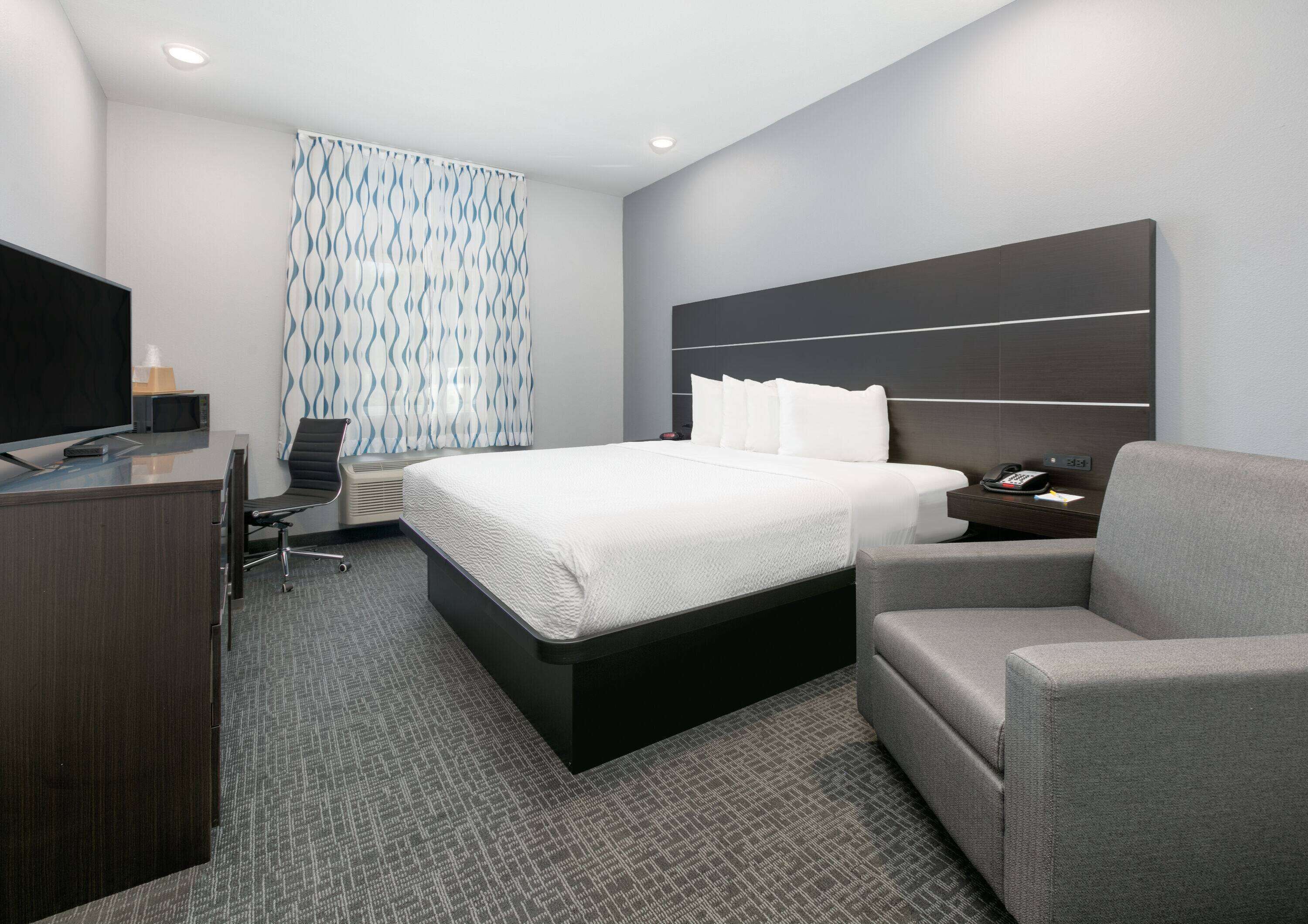 Quarto de hotel moderno com uma cama, escrivaninha, cadeira e televisão.