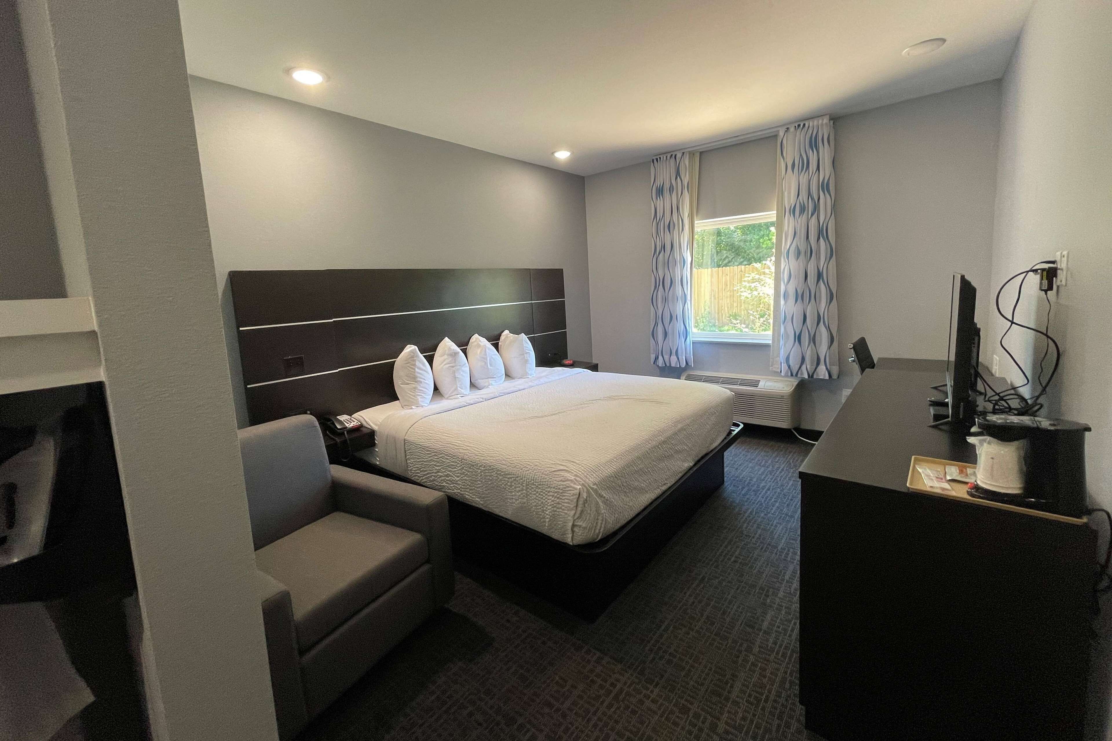 Une chambre d’hôtel avec un lit, un bureau, une chaise, une télévision et une fenêtre avec des rideaux.