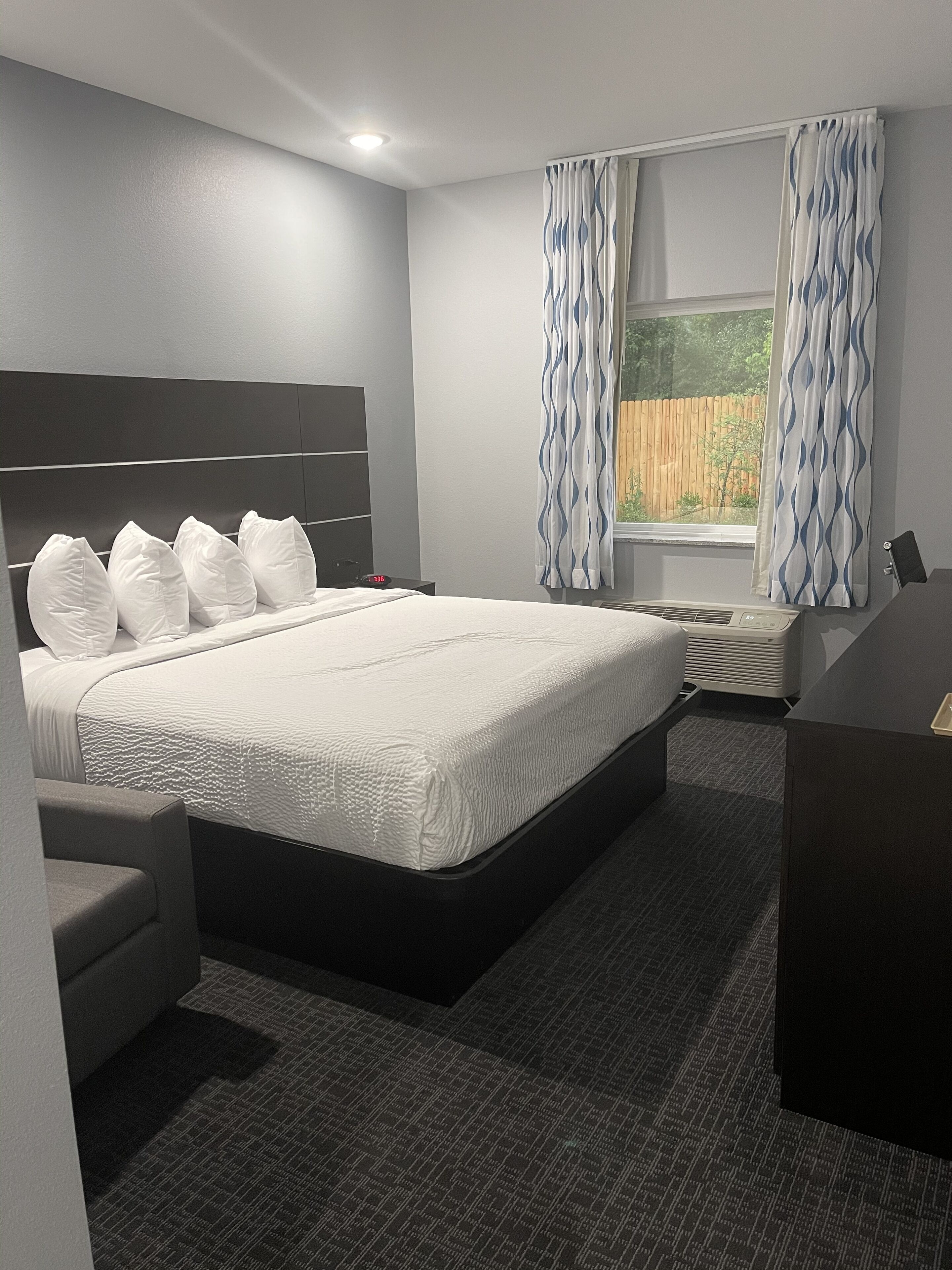 Una habitación de hotel moderna con una cama grande, una mesita de noche, una silla y una ventana con cortinas.