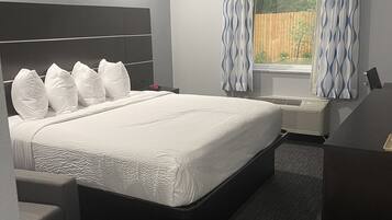 Una habitación de hotel moderna con una cama grande, una mesita de noche, una silla y una ventana con cortinas.