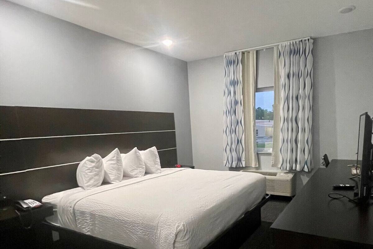 A hotel room with a large bed, a desk, a chair, and a window with curtains.