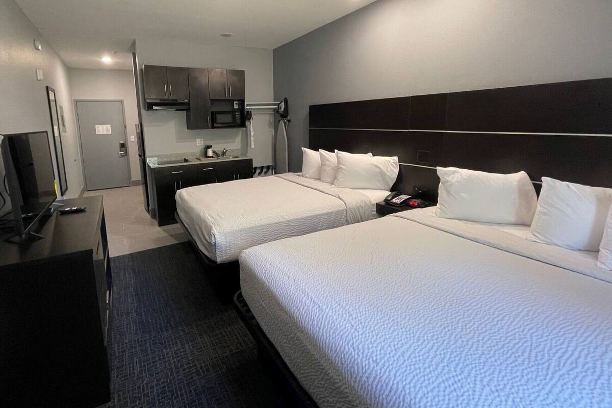 A hotel room with two beds, a desk, a TV, a microwave, and a small kitchenette.