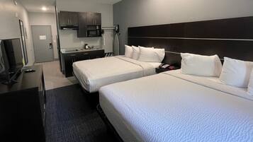 Quarto de hotel com duas camas, uma escrivaninha, televisão, micro-ondas e uma pequena copa.