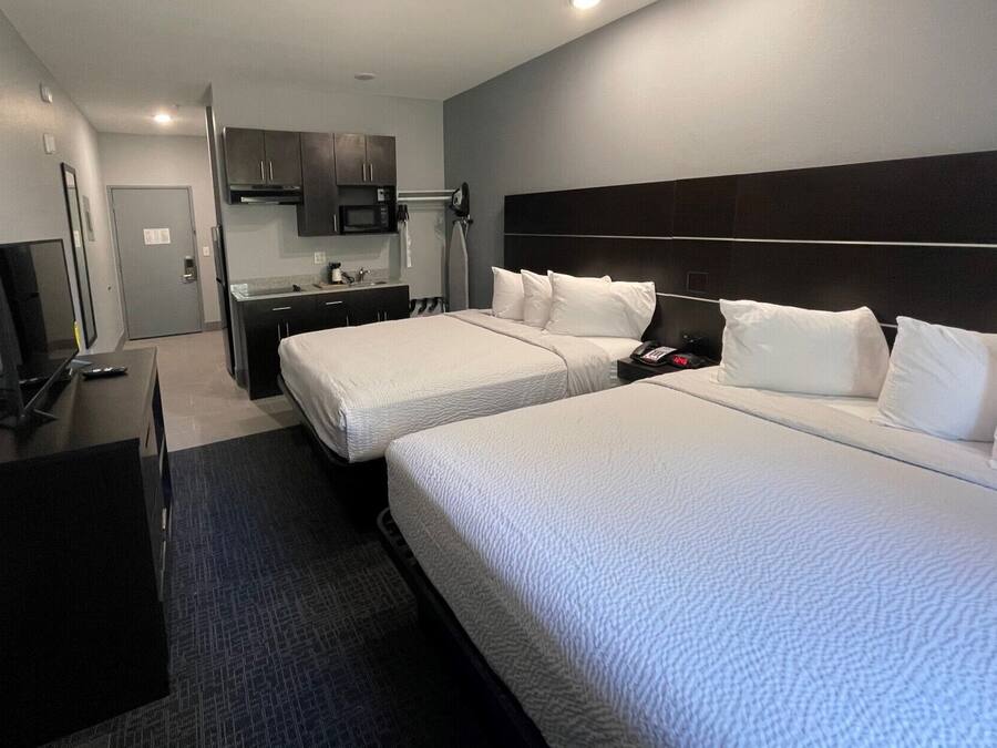 Quarto de hotel com duas camas, uma escrivaninha, televisão, micro-ondas e uma pequena copa.
