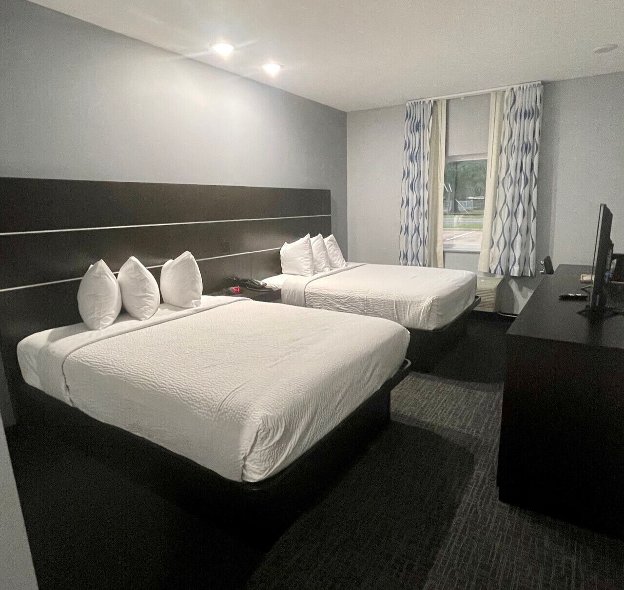 A hotel room with two beds, a desk, and a window with curtains.