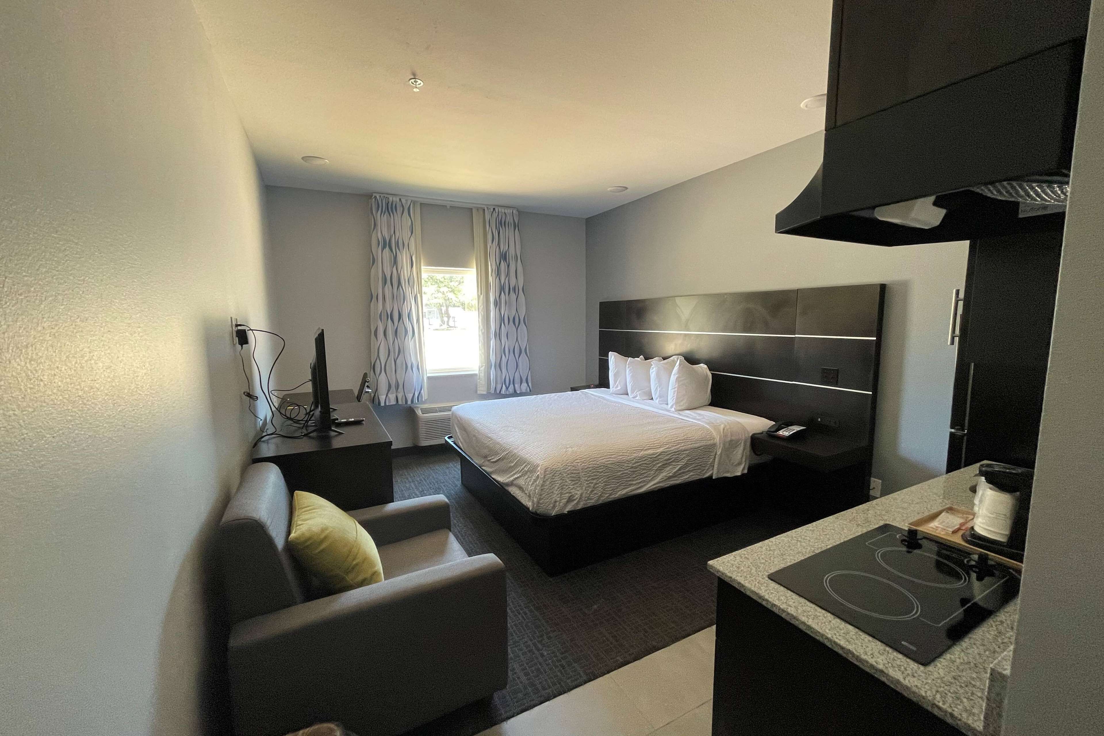 Habitación de hotel moderna con cama, sofá, escritorio con cafetera y estufa integrada.