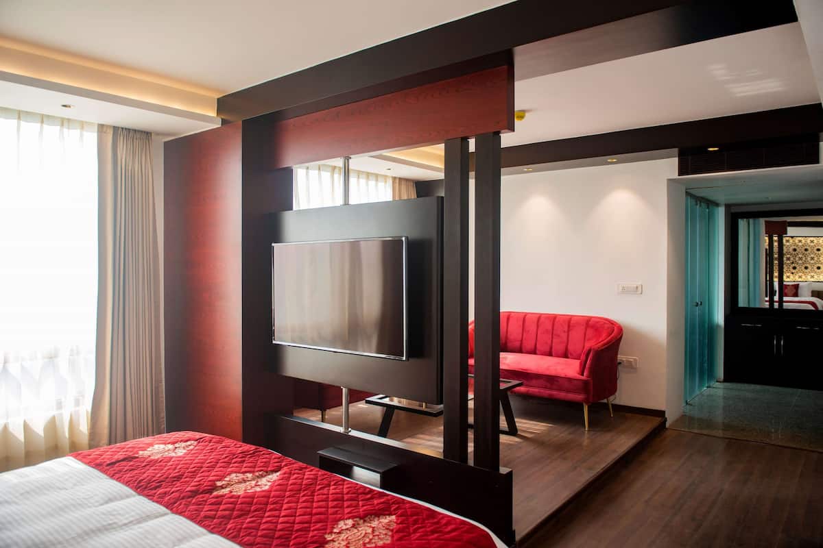 Et moderne hotelværelse med en stor seng, et fladskærms-tv, en rød sofa og trægulv.