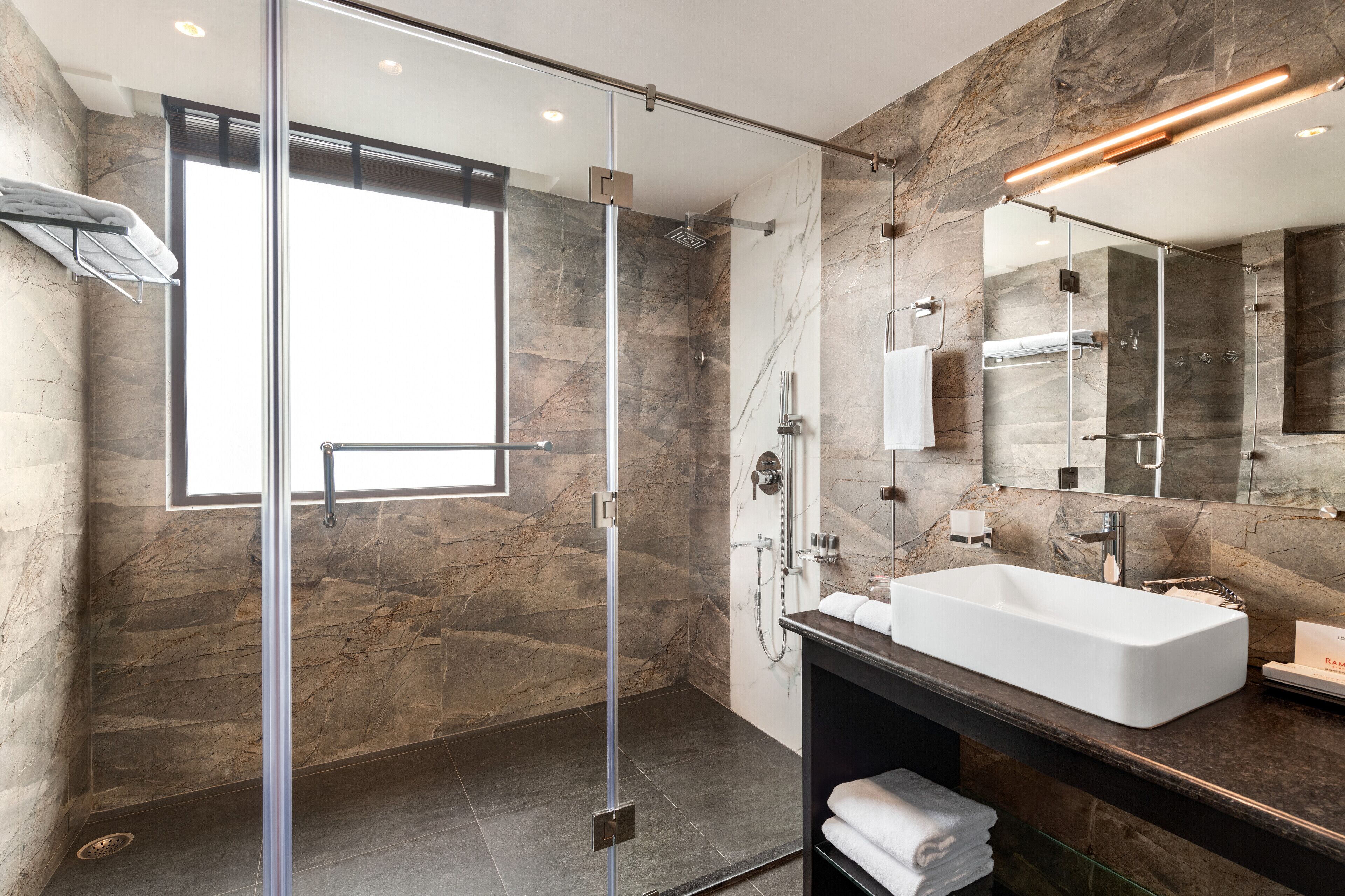 A modern bathroom with a glass-enclosed shower, a large mirror, and a marble-tiled wall.