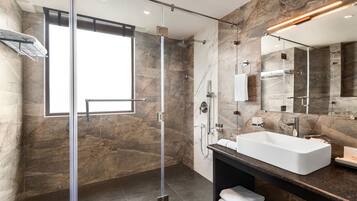 A modern bathroom with a glass-enclosed shower, a large mirror, and a marble-tiled wall.