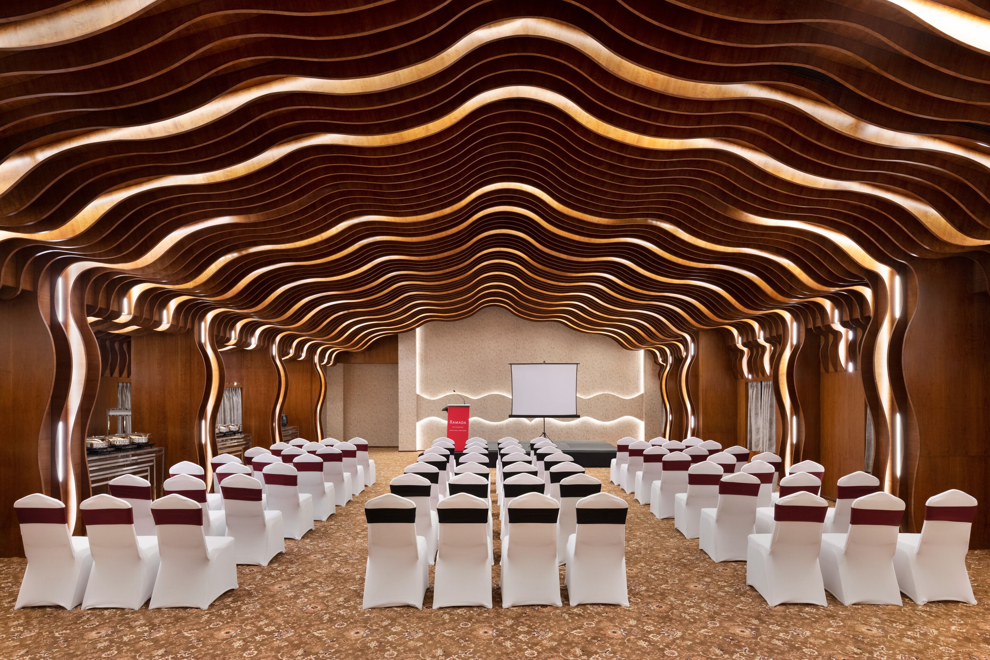 A conference room with rows of white chairs, a podium, and a screen at the front.