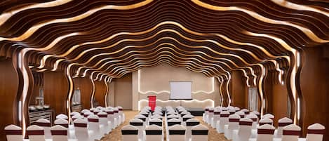A conference room with rows of white chairs, a podium, and a screen at the front.
