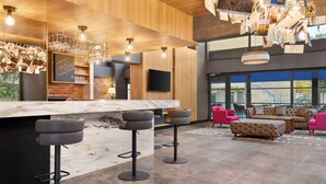 Un área de bar moderna con mostrador de mármol, taburetes negros y techo de madera con lámparas colgantes.