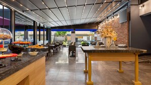 Un restaurante moderno con una barra larga, varias zonas de estar y un arreglo decorativo de plantas.