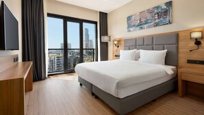 Una habitación de hotel moderna con una cama grande, un escritorio y un balcón con vistas a la ciudad.
