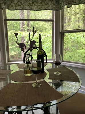 Una mesa de comedor con cubierta de vidrio, rodeada de individuales tejidos, una botella de vino y una copa de vino tinto.