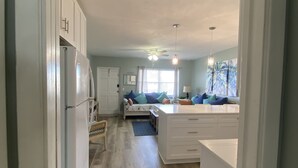 Uma cozinha moderna com armários brancos, frigorífico embutido e um espaço de refeições com banco e almofadas.