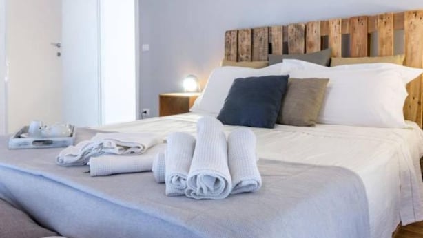 Un lit bien fait, avec des serviettes pliées, une tête de lit en bois et une table de chevet avec une lampe.