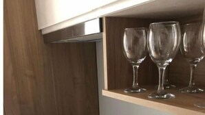 Une cuisine moderne dotée d’une cuisinière intégrée, d’une étagère en bois où sont rangés des verres à vin, et d’un plateau avec des tasses et des soucoupes à thé.