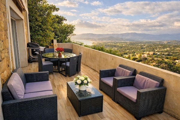 A balcony with wicker furniture, a glass table, and a vase of flowers.
