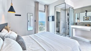Habitación de hotel moderna con una cama grande, un baño con cabina de ducha de vidrio y un balcón con vistas.