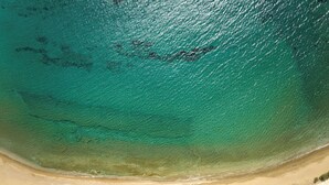 Vista aérea de una playa con aguas turquesas cristalinas, orilla de arena y vegetación escasa.