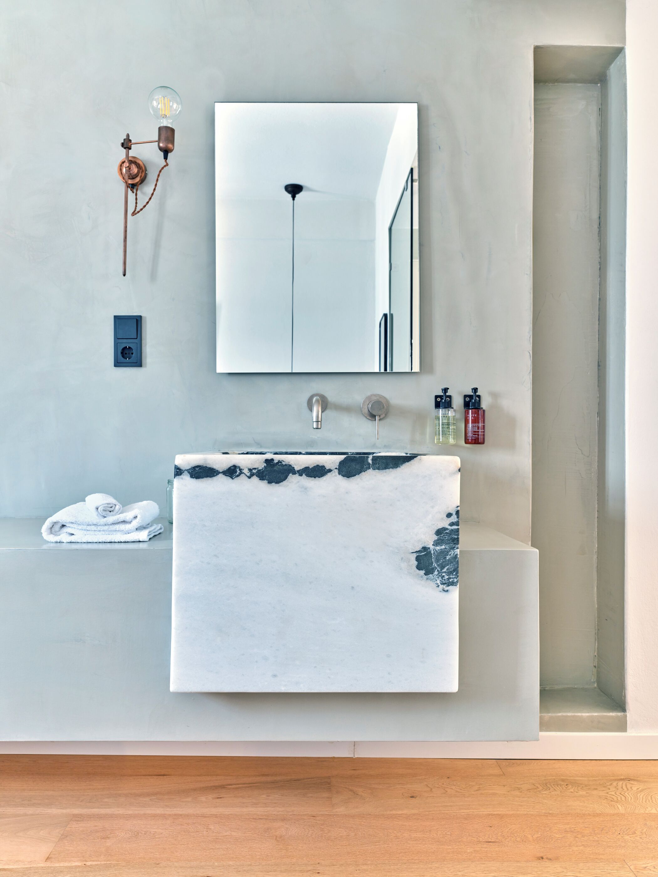 Une salle de bain avec un lavabo en marbre, une serviette, un miroir et un luminaire.