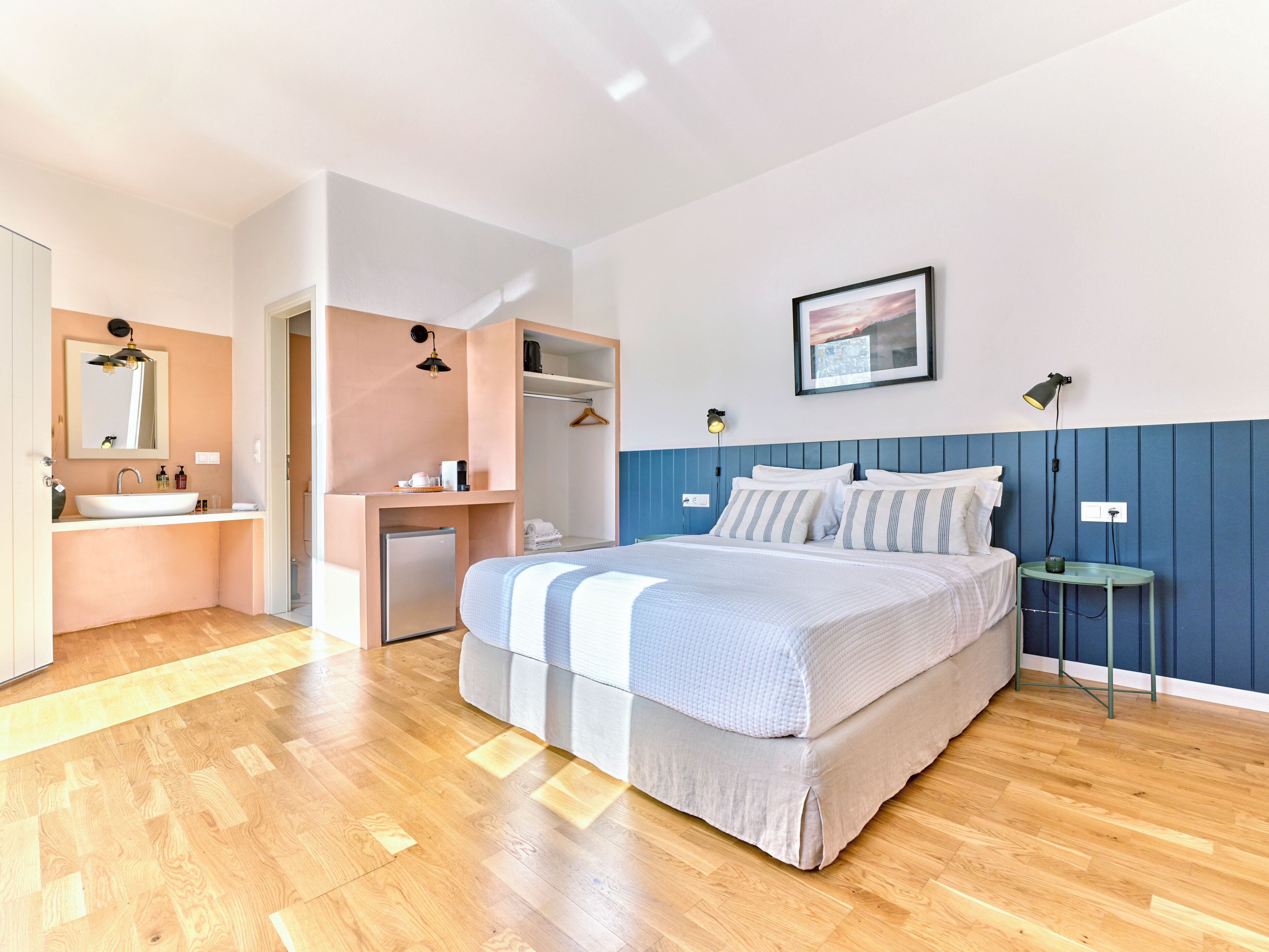 A modern bedroom with a large bed, a built-in wardrobe, a small desk, and a bedside table with a lamp.