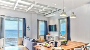 Una sala de estar moderna con una mesa de comedor de madera, sillas blancas, un sofá gris y un televisor montado en la pared.