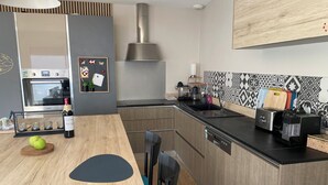 A modern kitchen with a built-in oven, a stainless steel range hood, a toaster, and a coffee machine. - Comfortable villa **** for 6 with swimming pool at walking distance from the sea (Gujan-Mestras)