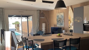 A modern kitchen with a central island, bar stools, a dining table, and a view of an outdoor pool. - Comfortable villa **** for 6 with swimming pool at walking distance from the sea (Gujan-Mestras)