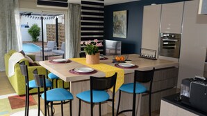 A modern kitchen with a dining area, featuring a central island with bar stools, a built-in oven, and a view of the outdoor patio. - Comfortable villa **** for 6 with swimming pool at walking distance from the sea (Gujan-Mestras)