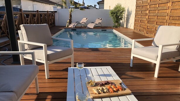 A wooden deck with a pool, white lounge chairs, and a table with food and drinks. - Comfortable villa **** for 6 with swimming pool at walking distance from the sea (Gujan-Mestras)