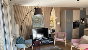 A modern living room with a TV, seating, and a kitchen area. - Comfortable villa **** for 6 with swimming pool at walking distance from the sea (Gujan-Mestras)
