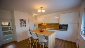A modern kitchen with white cabinets, a wooden island with chairs, and a built-in oven. - Villa Vida (Zmijavci)
